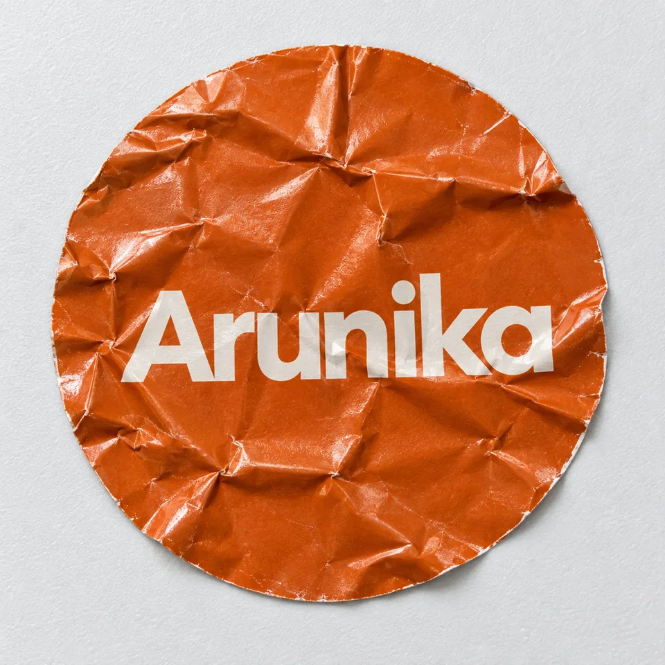 Foto makro tegak lurus satu stiker vinyl bulat {{primary_color}} berlogo {{brand_name}} yang kusut parah, lipatan tajam